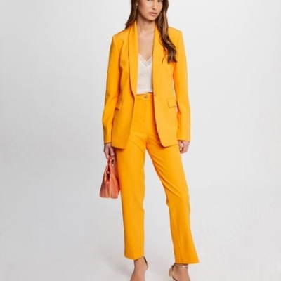 Mulher vestindo fato amarelo com blusa branca e sandálias douradas, bolsa rosa, fundo branco