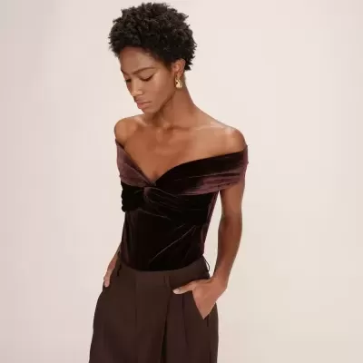 Mulher com body de veludo castanho e calças castanhas largas, fundo bege neutro