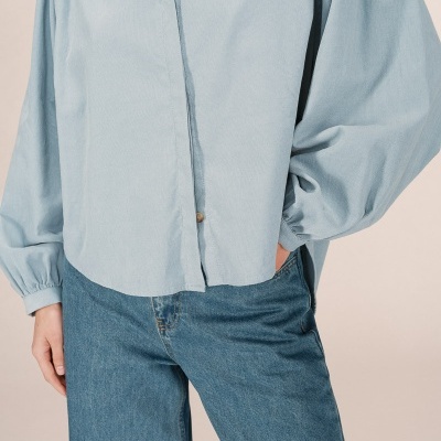 Camisa azul claro de tecido leve com mangas compridas e punhos franzidos e calças de ganga azul