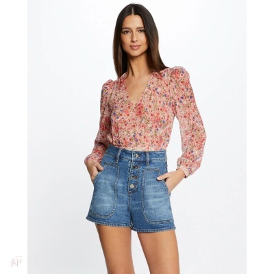 Mulher com blusa rosa florescida e shorts curtos de ganga azul