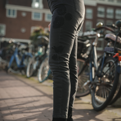 Calças justas pretas com padrão de flores pretas, em ambiente urbano com bicicletas ao fundo