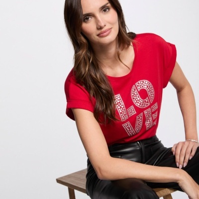Mulher sentada com camiseta vermelha  LOVE e calças pretas