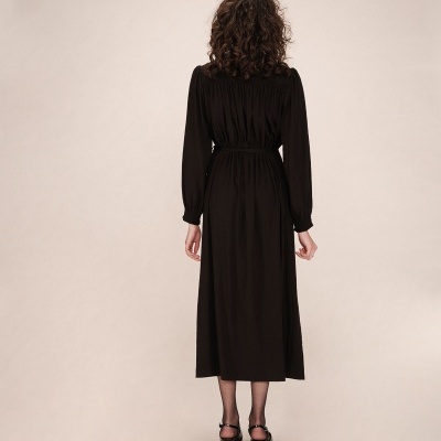 Vestido preto comprido de costas com sandálias pretas em fundo bege