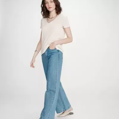 Mulher com t-shirt bege e calças de ganga azuis em fundo branco