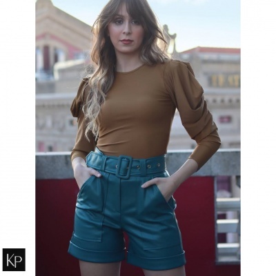 Mulher com blusa castanha e calções verdes escuros com cinto em ambiente urbano