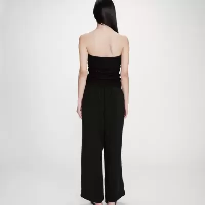 Mulher vista de costas com top tomara-que-caia e calças largas pretas.