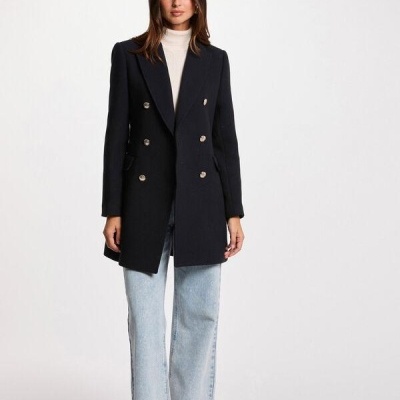 Casaco preto de lã com botões dourados, mulher com jeans claros e sapatilhas azuis e brancas