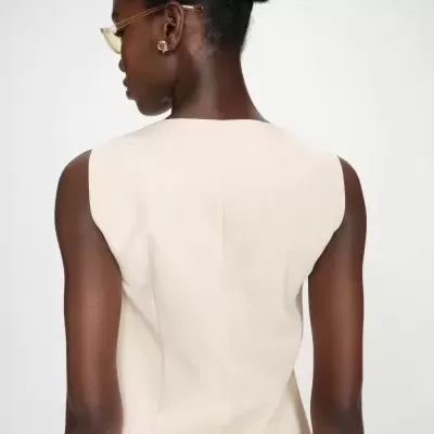 Mulher de costas com vestido bege sem mangas e acessórios dourados