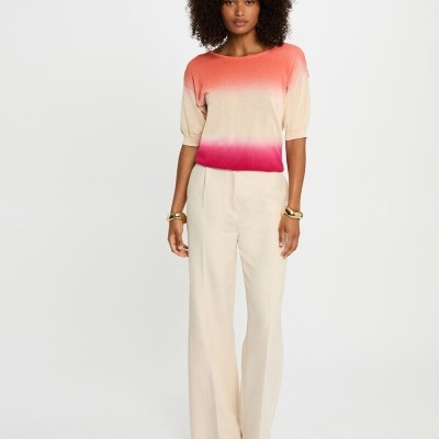 Mulher com camisola ombré coral/bege/rosa, calças largas bege e sandálias abertas.