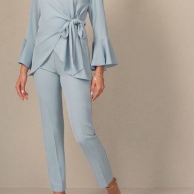 Conjunto feminino azul claro com camisa de mangas longas e calças justas, sapatos de salto dourados.