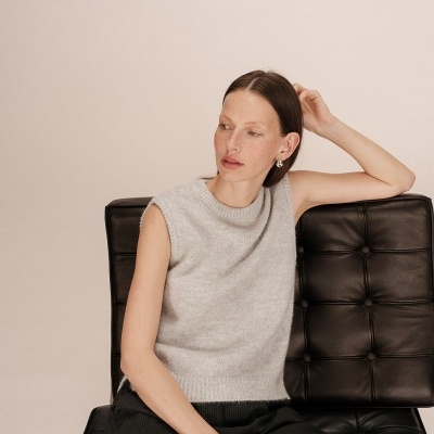 Mulher com colete de malha cinza claro e calças pretas sentada numa cadeira de couro preta.