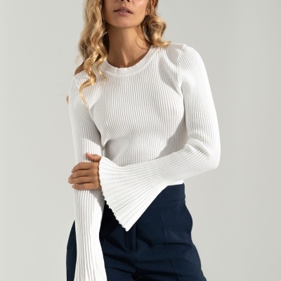 Mulher vestindo camisola branca de malha canelada com mangas largas e calças escuras