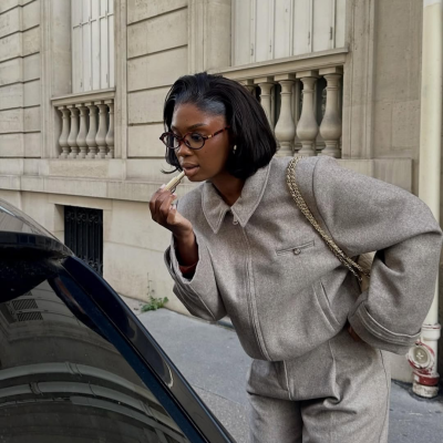 Mulher a aplicar batom numa rua com edifício de pedra ao fundo