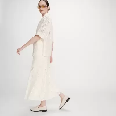 mulher com vestido e saia branca rendada, sapatos brancos e óculos de sol castanhos