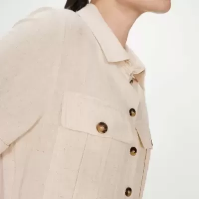 Camisa bege claro de linho com botões castanhos e bolsos no peito, vista lateral