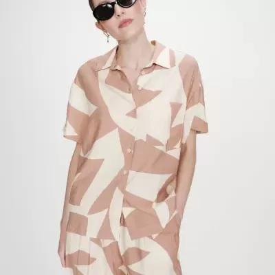 Conjunto de roupa bege e creme com padrão abstrato, camisa e calças, mulher com óculos escuros.