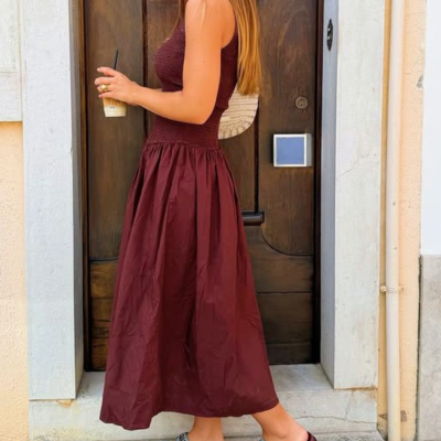 Mulher com vestido bordô e sandálias desportivas junto a porta de madeira
