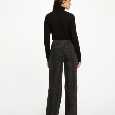 Mulher de costas a usar calças largas cinza escuro com padrão e camisola preta de gola alta.