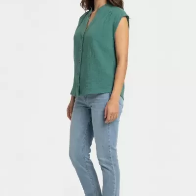 Mulher com blusa verde sem mangas, calças de ganga azuis e ténis bege