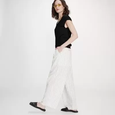 Mulher a usar calças brancas às riscas e top preto, com óculos de sol amarelos