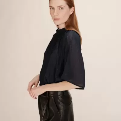 Mulher com blusa preta semitransparente e saia preta de pele em fundo bege