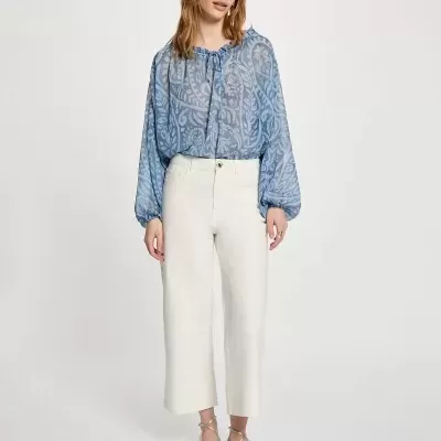 Mulher vestindo blusa azul com padrão floral e calças brancas cropped.