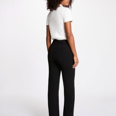 Pessoa de costas com camisa branca manga curta, calças pretas e sapatos pretos de salto.