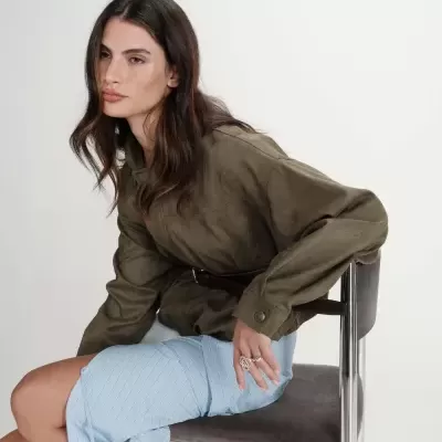 Mulher sentada com casaco verde-militar e saia azul claro às riscas