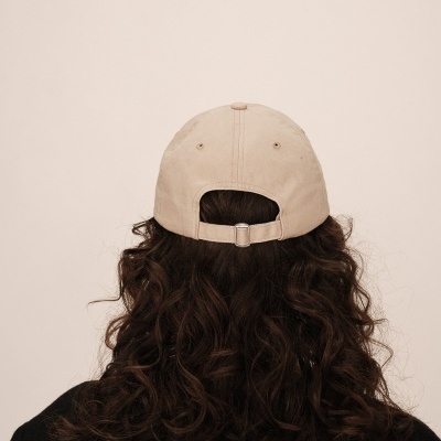 Boné bege visto por trás, cabelo castanho ondulado, roupa preta