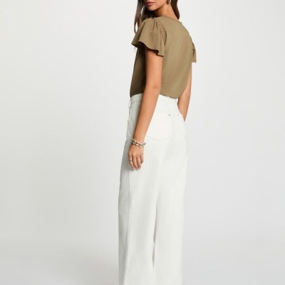 Mulher com blusa kaki e calças brancas largas vista de costas em fundo branco