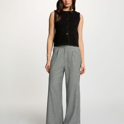 Mulher com colete preto e calças xadrez preto e branco num fundo branco