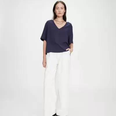 Mulher com blusa azul escuro e calças brancas largas