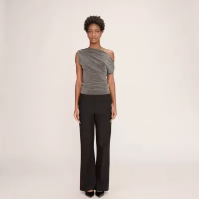 Mulher com blusa cinza assimétrica e calças pretas em fundo claro.