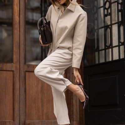 Mulher de casaco bege, calças bege e sapatos de salto pretos com mala castanha escura