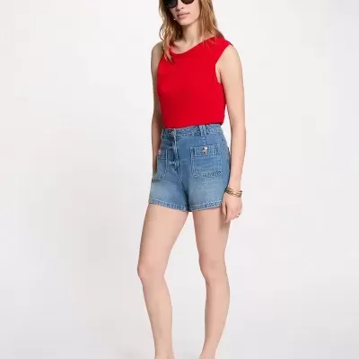 Mulher com tshirt vermelha, calções de ganga e sapatos rasos bege com fundo branco.