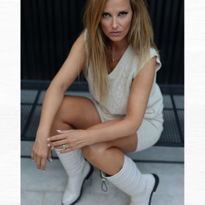 Mulher com colete de malha bege e botas brancas sentada