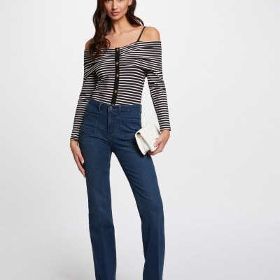 Mulher com camisa de riscas horizontais pretas e brancas, calças de ganga azuis e sandálias douradas segurando carteira branca