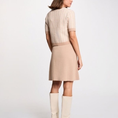 Mulher com blusa de malha bege e saia bege, botas brancas, vista de costas