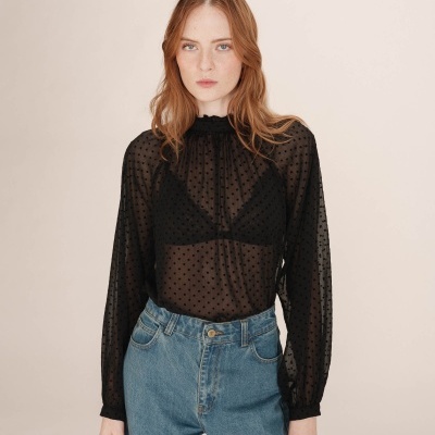 Blusa preta transparente com bolinhas e calças de ganga azuis.