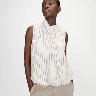 Blusa branca com riscas finas verticais e laço na gola usada por mulher