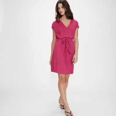 Mulher com vestido rosa fúcsia e sandálias pretas num fundo branco.