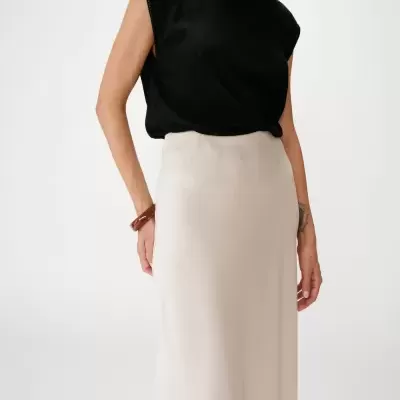 Mulher com blusa preta sem mangas e saia comprida bege em fundo branco