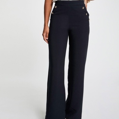 Calças pretas largas com botões dourados e sapatos brancos