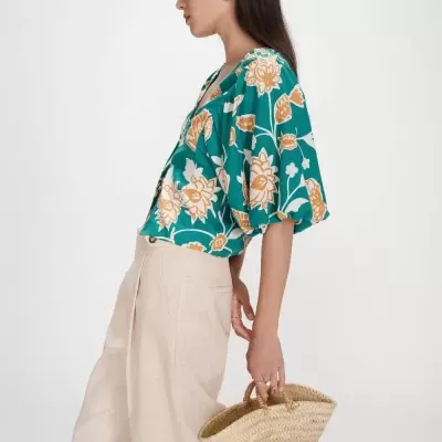 Mulher com blusa floral verde, calças bege e bolsa de palha