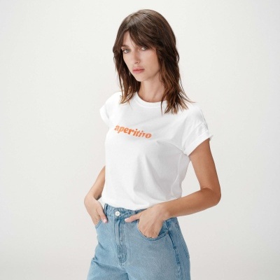 Mulher com t-shirt branca com texto laranja aperitivo e calças de ganga azuis