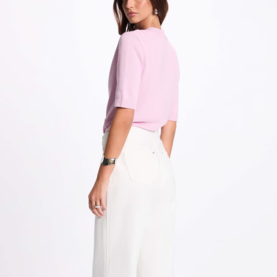 Mulher com camisola rosa e calças brancas em fundo branco