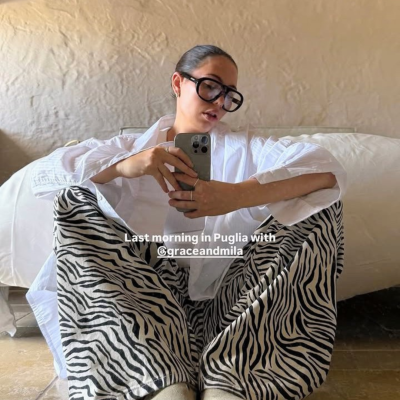 Mulher com calças zebras preto e branco, camisa branca e óculos grandes sentado no chão