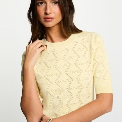 Camisola amarela com padrão LOVE em malha fina, usada por mulher com calças jeans cinza.
