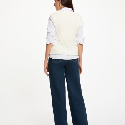 Mulher de costas com camisa branca, colete branco texturizado e calças de ganga largas azuis