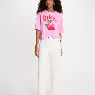 Mulher com t-shirt rosa com estampa de morango e calças brancas em fundo branco